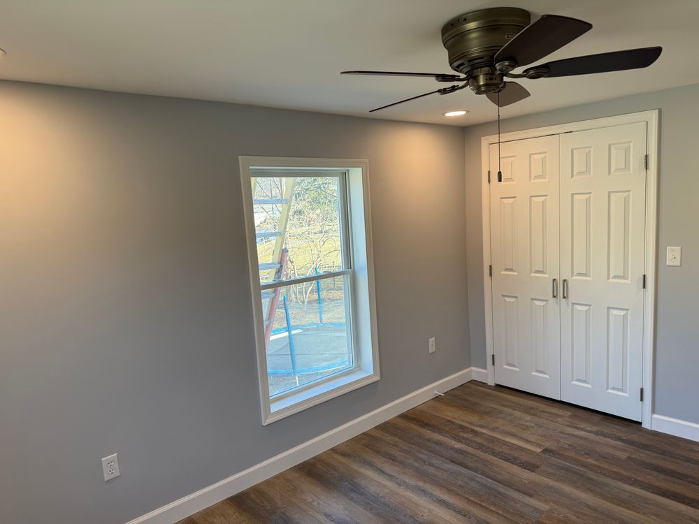 An interior shot of a room with light grey walls, white trim, wood-look flooring, a window, and a white double door.