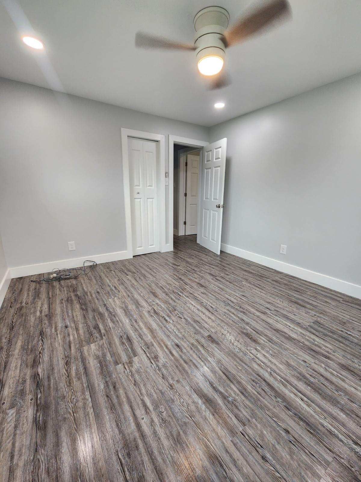 An empty room with light gray walls, dark wood-look laminate flooring, a ceiling fan, and two white doors.