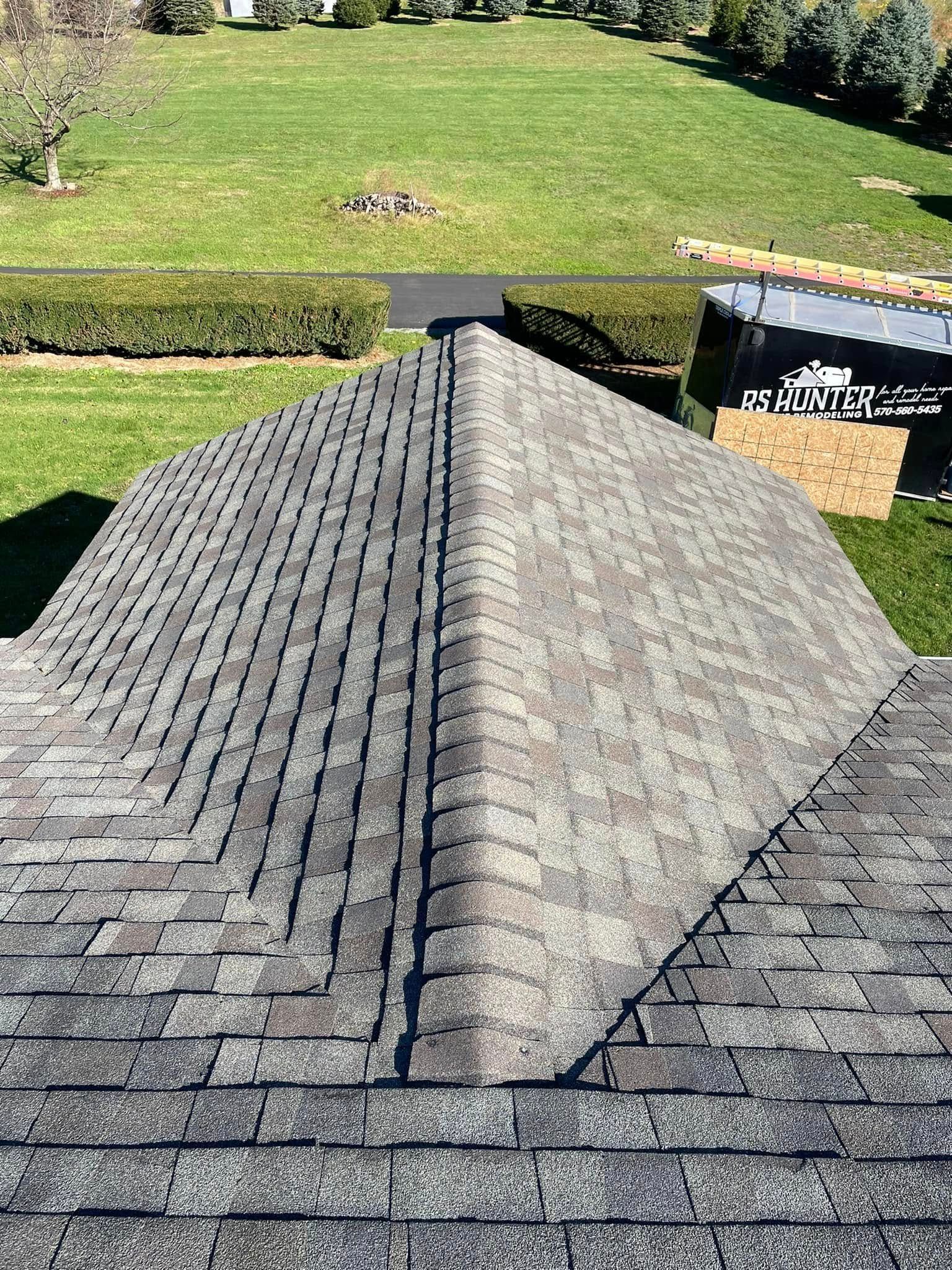 A high-angle view of a residential roof showing two different gray asphalt shingle patterns meeting at a center ridge.