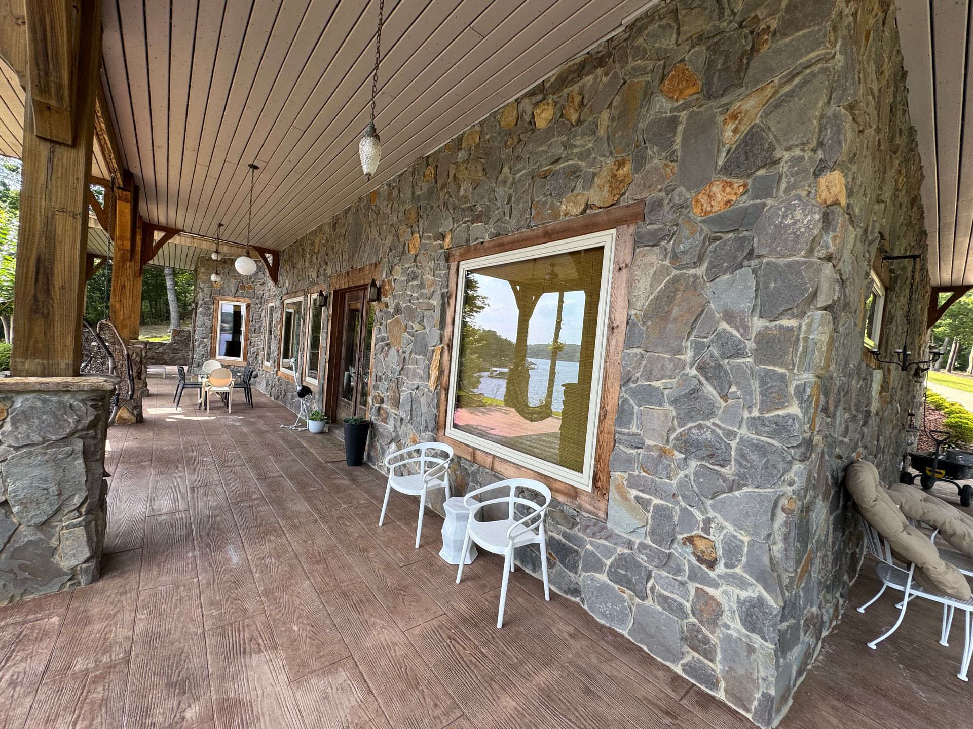 Covered porch with stone wall and several white chairs.