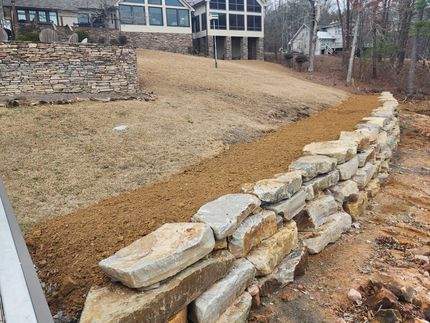 Stone retaining wall with a graded hillside and a house in the background.