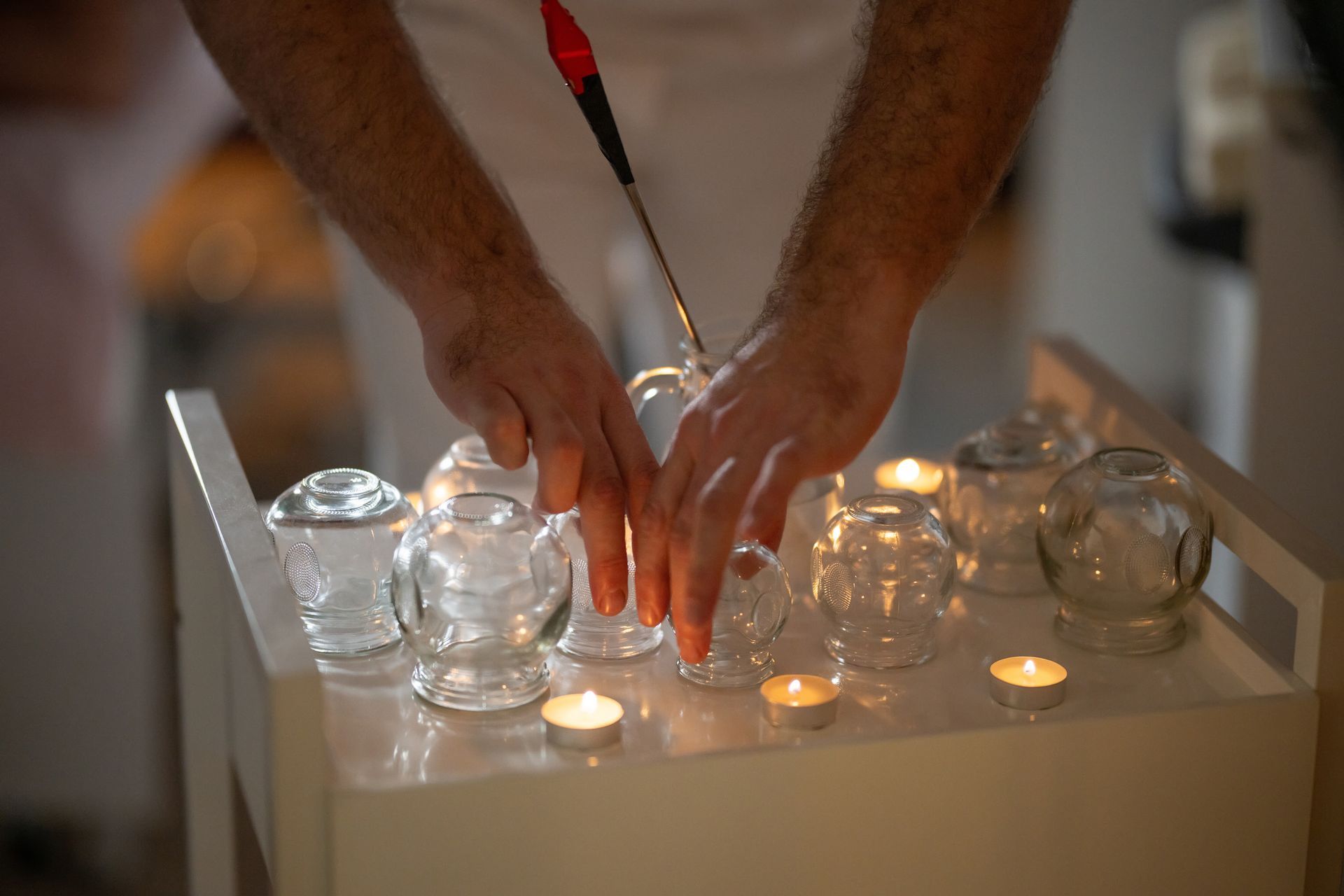 Hands arranging glass cups with lit candles, preparing for cupping therapy.