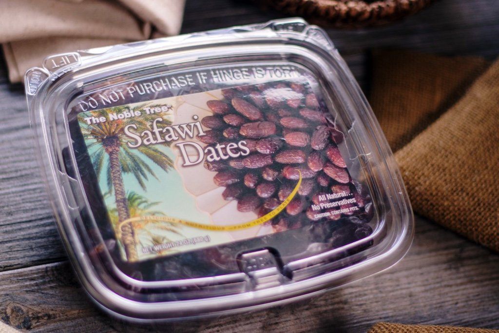 A plastic container filled with dates is sitting on a wooden table.