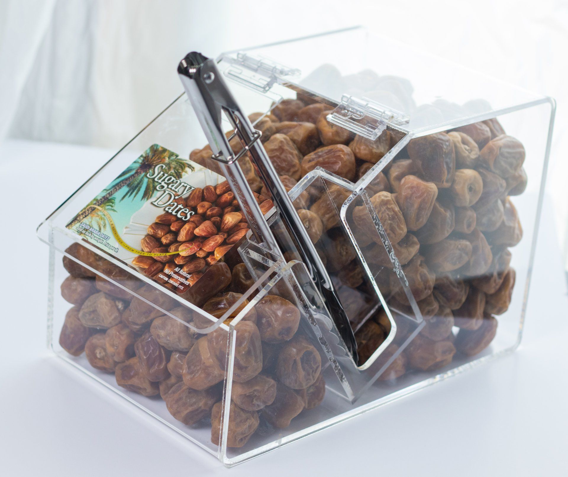 A clear container filled with nuts and a tong