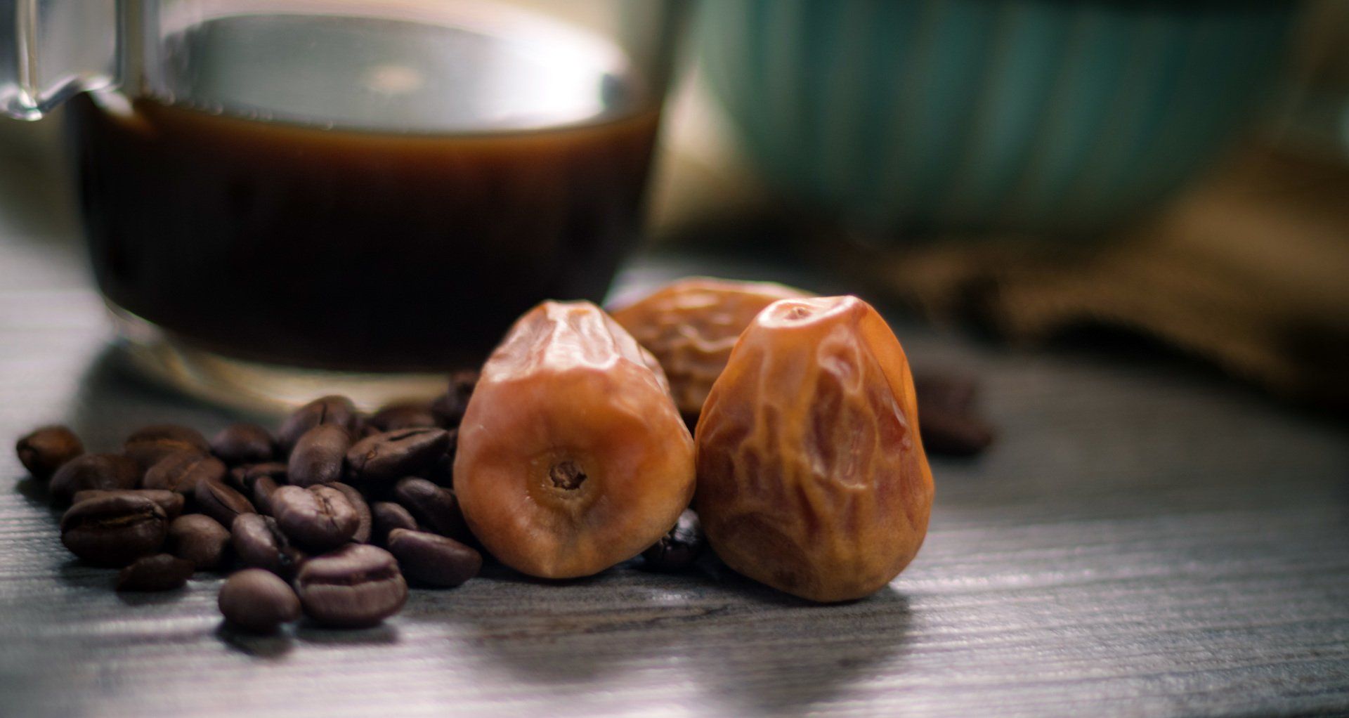 A cup of coffee , dates and coffee beans on a table.
