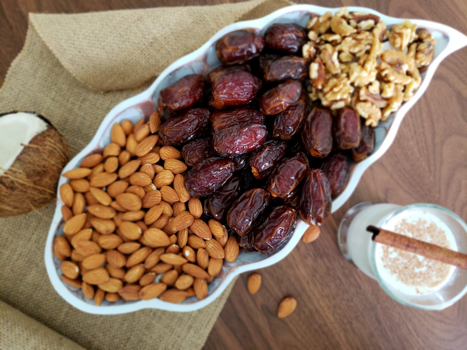 A white bowl filled with dates , almonds , walnuts and coconut.