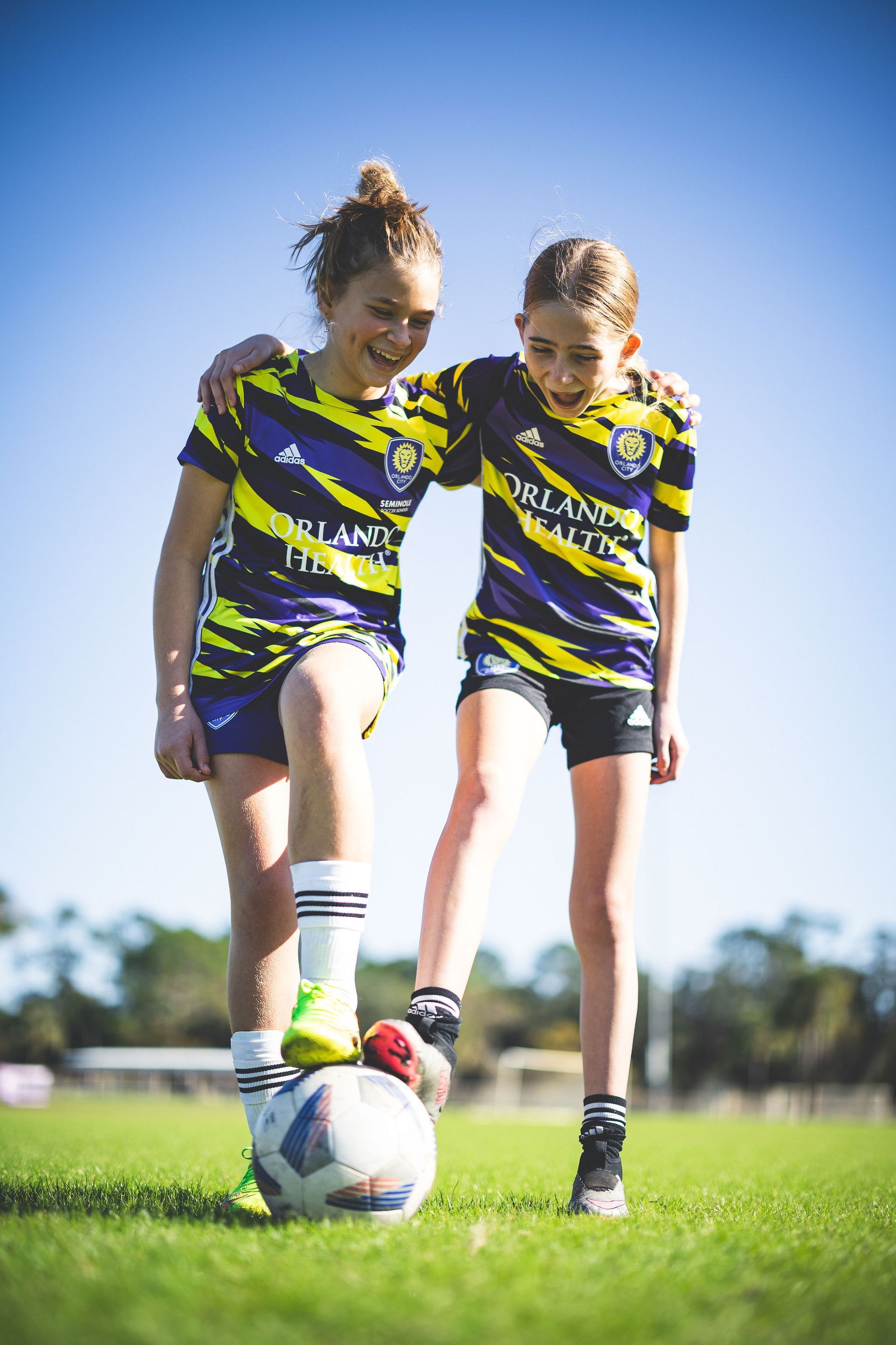 Two female soccer players side by side with their feet on a soccer ball