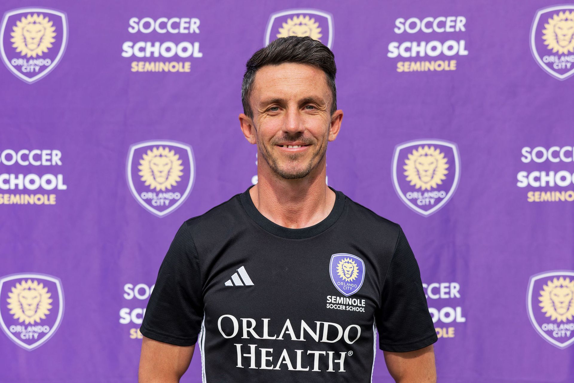 A headshot of someone called Lewis Neal. He is standing against a purple wall