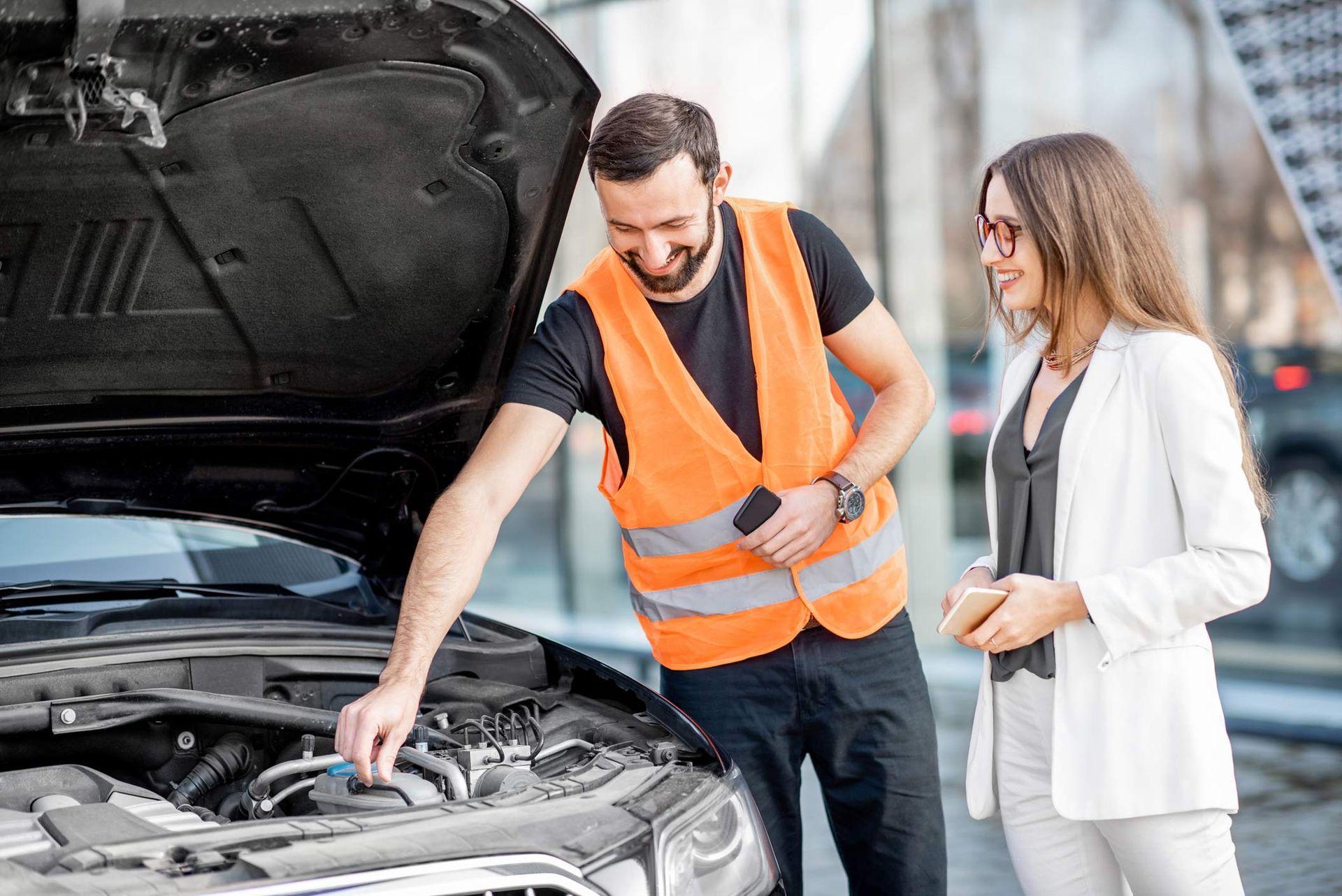 A man and a woman are looking under the hood of a car.