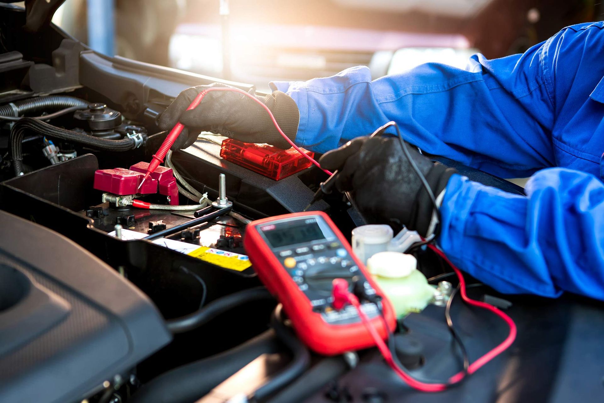 A mechanic is working on a car battery with a multimeter.