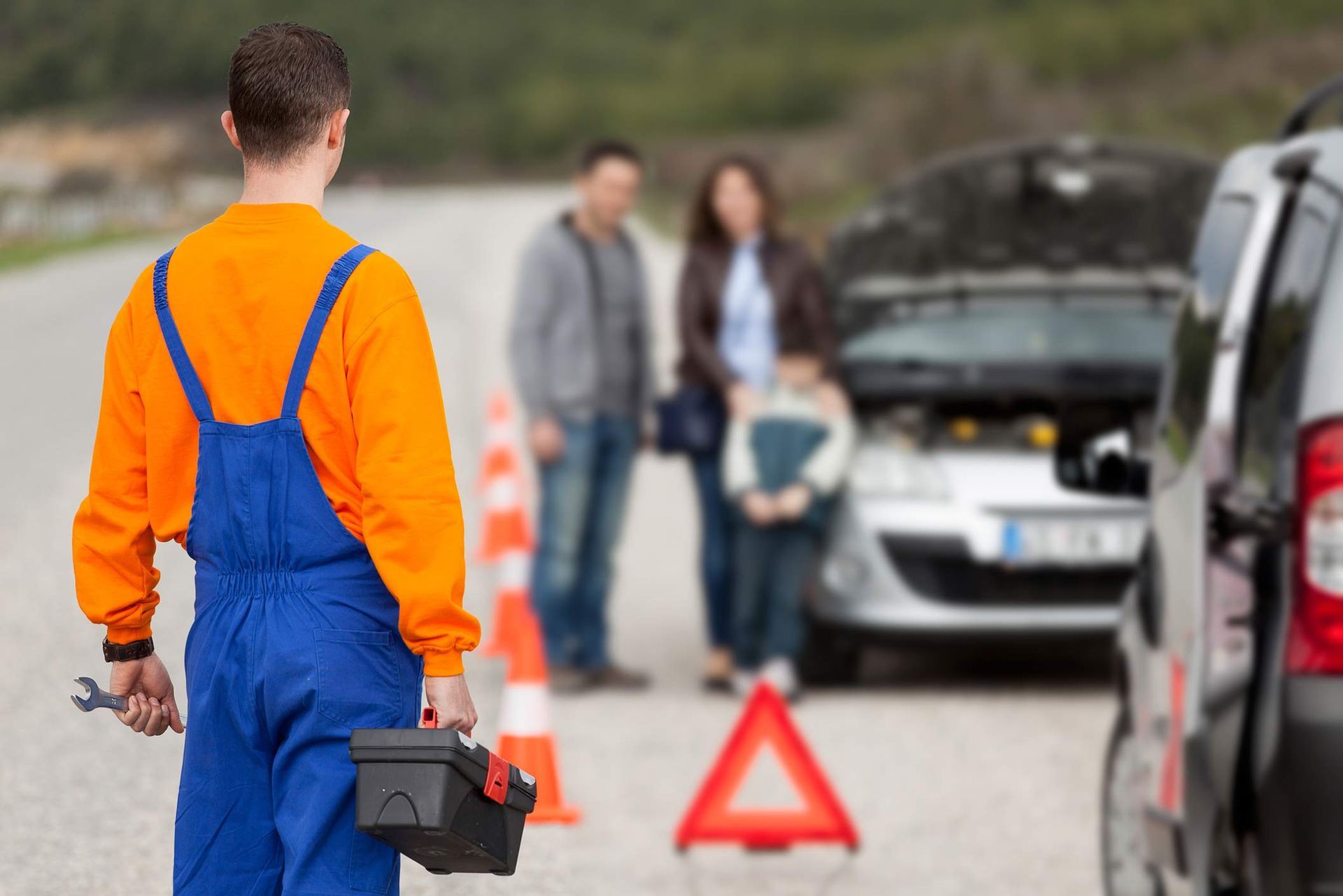 A man is standing next to a broken down car on the side of the road.
