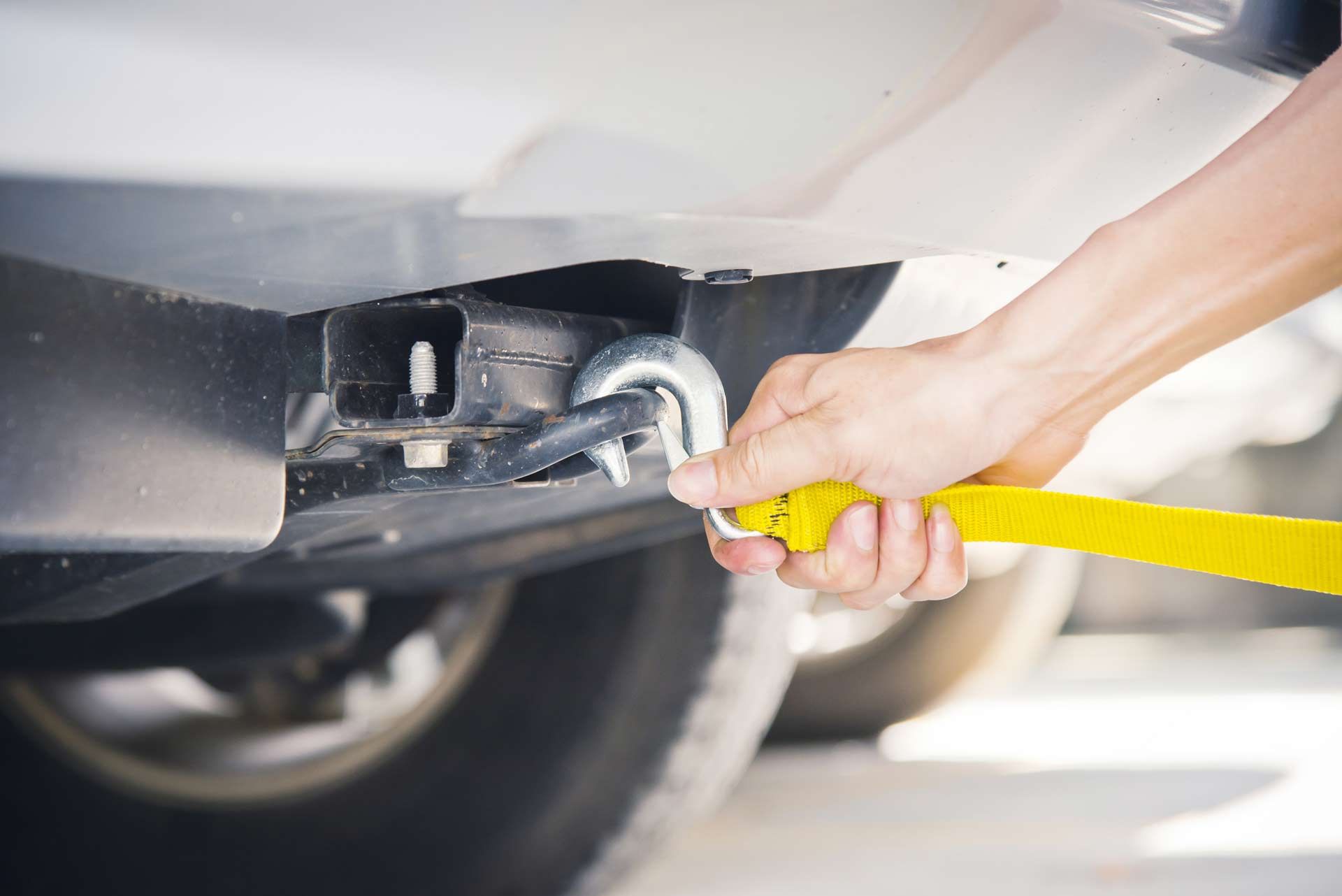 A person is towing a car with a yellow tow strap.