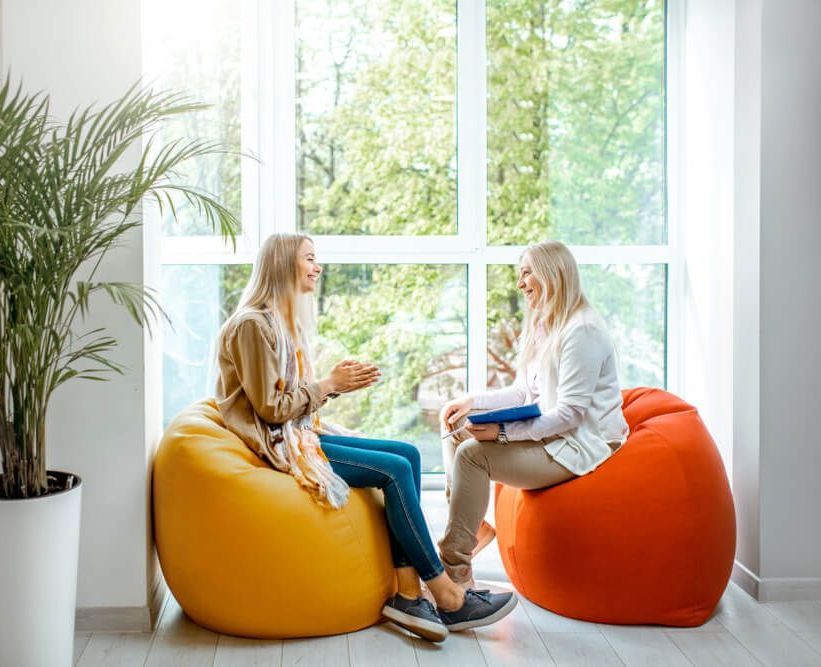 Two women are sitting on bean bag chairs in front of a window — Hands on Healing Massage In Tamworth, NSW