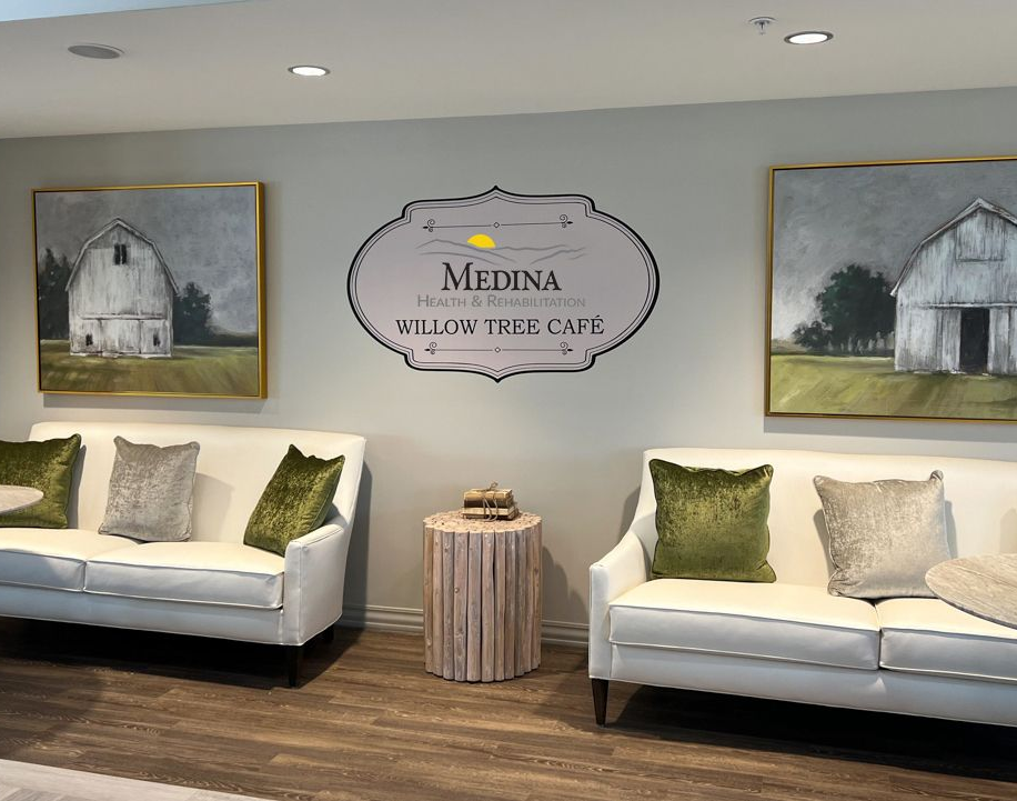 Two white sofas with throw pillows flank a logo above a round side table, with barn paintings on the wall.