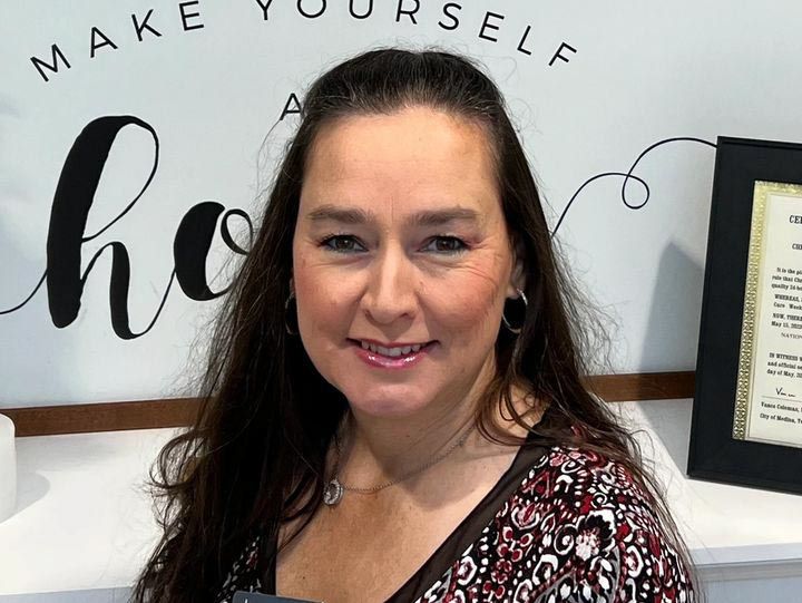 Woman smiling, dark hair, in front of a wall with