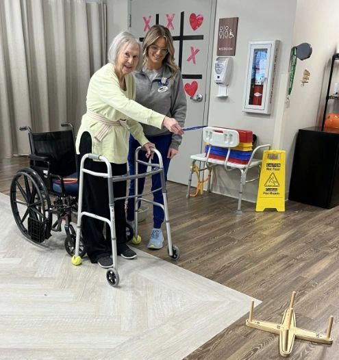 Elderly woman and caregiver playing game in a room. Woman uses a walker and points.