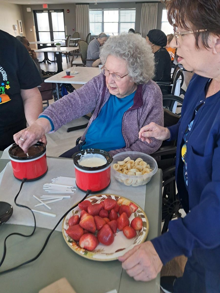 People at a table dipping strawberries, bananas into chocolate and white cream using fondue pots.