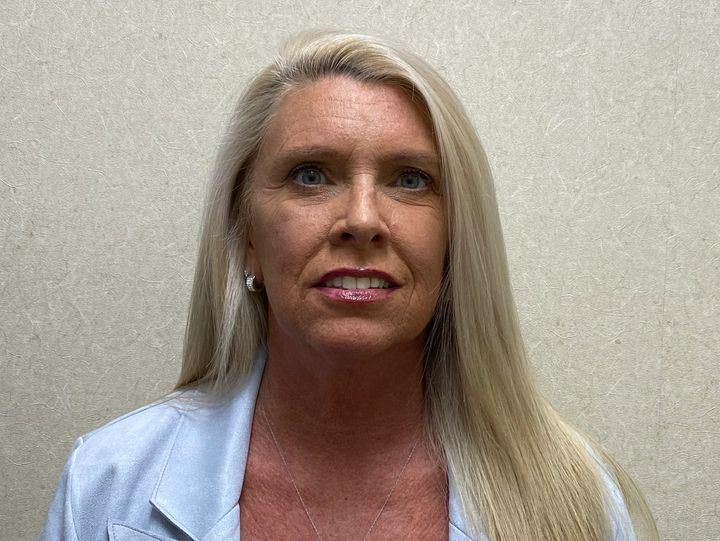 Woman with long blonde hair wearing a light blue coat, facing the camera.