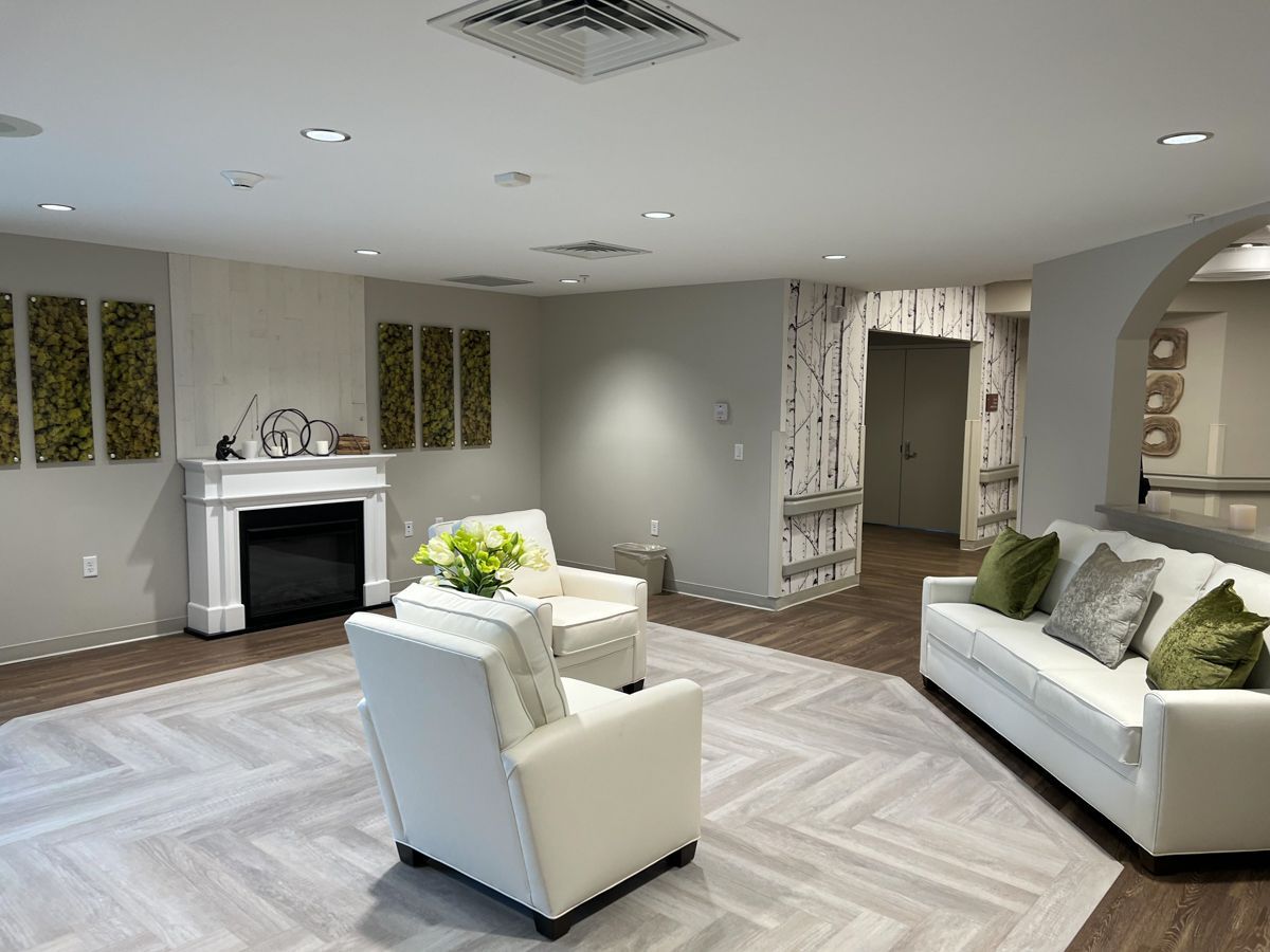 Lounge area with fireplace, white furniture, and decorative wall art; light gray and beige tones.