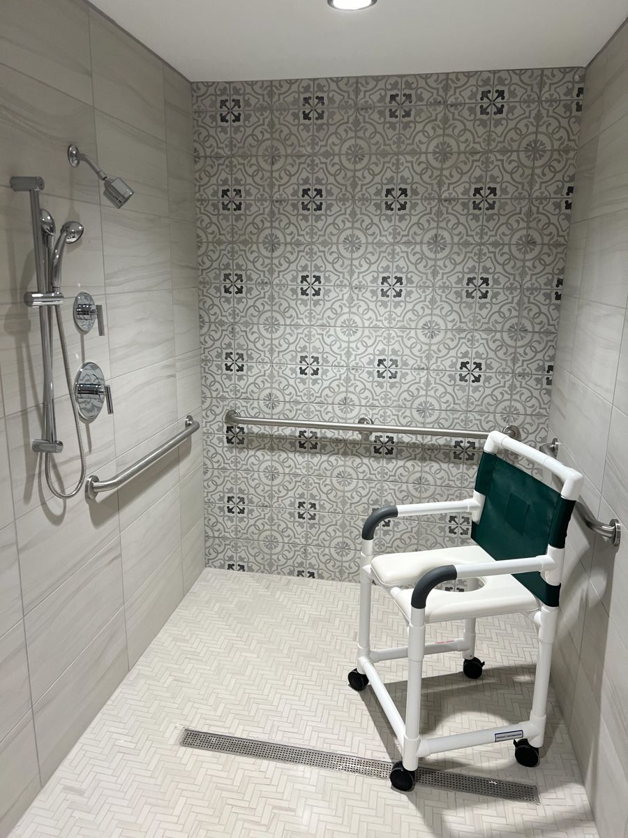 Accessible shower with tile, handrails, shower chair, and showerhead.