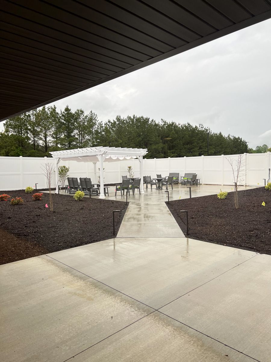 Outdoor patio with seating, white fence, and pathway, under a dark overhang on a rainy day.