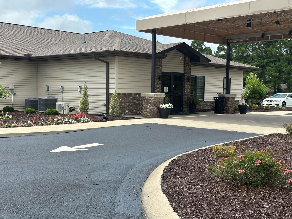 Drive-through bank with a dark asphalt driveway, brown landscaping, and a beige building with a dark roof.