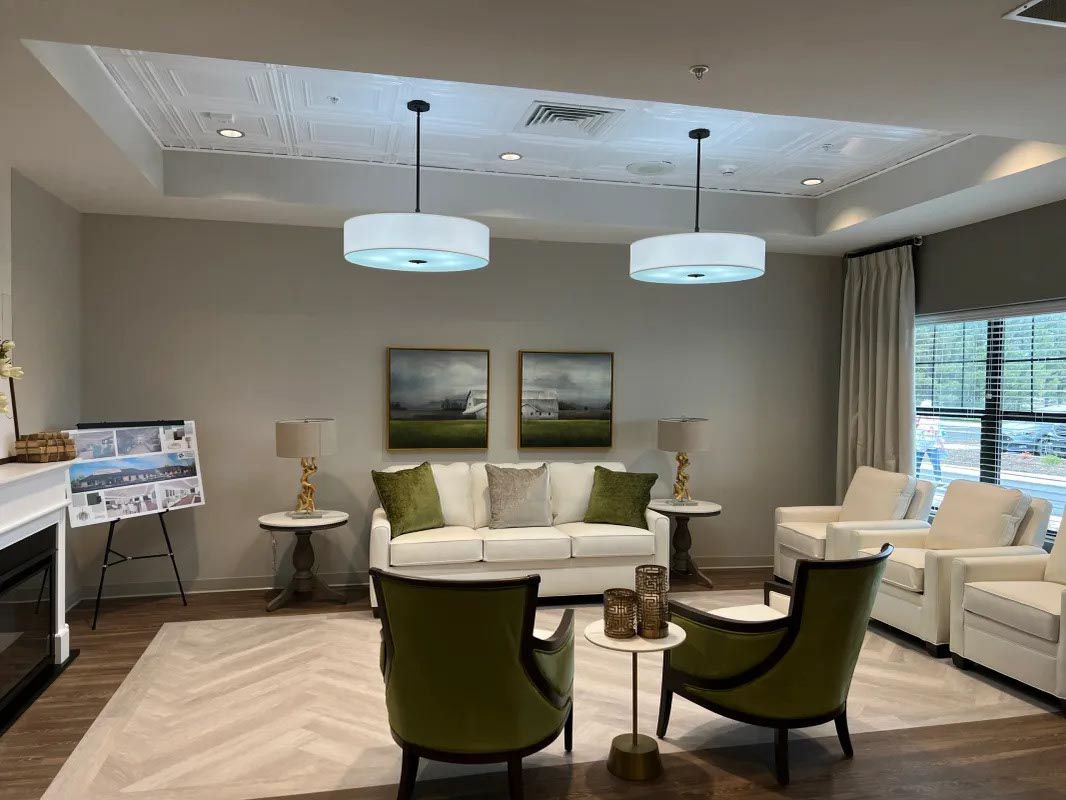 A well-lit lounge with white furniture, green chairs, art, pendant lights, and a fireplace.