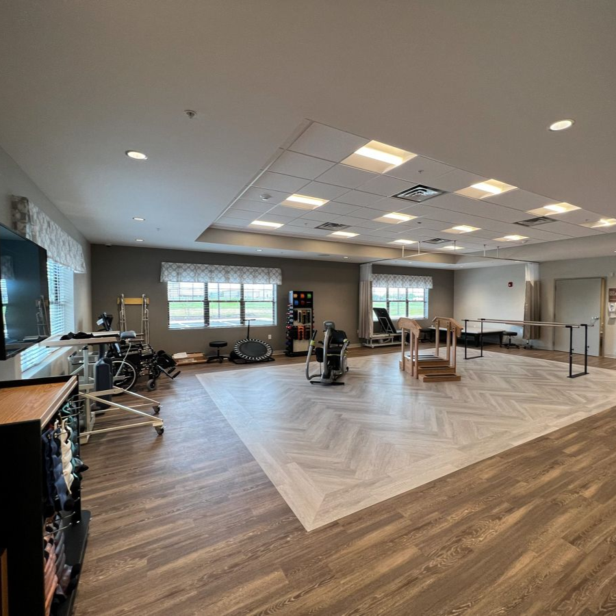 Rehab gym with exercise equipment, windows, and wood-look flooring.