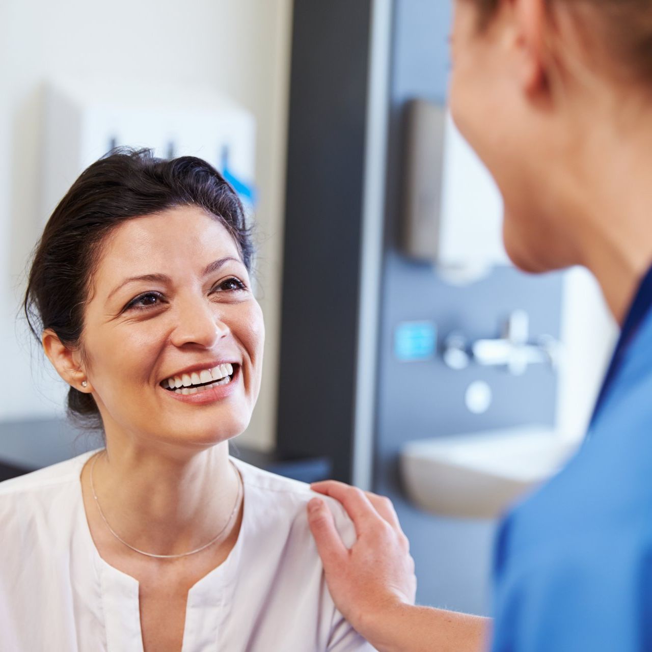 Woman smiles while a medical professional touches her shoulder.