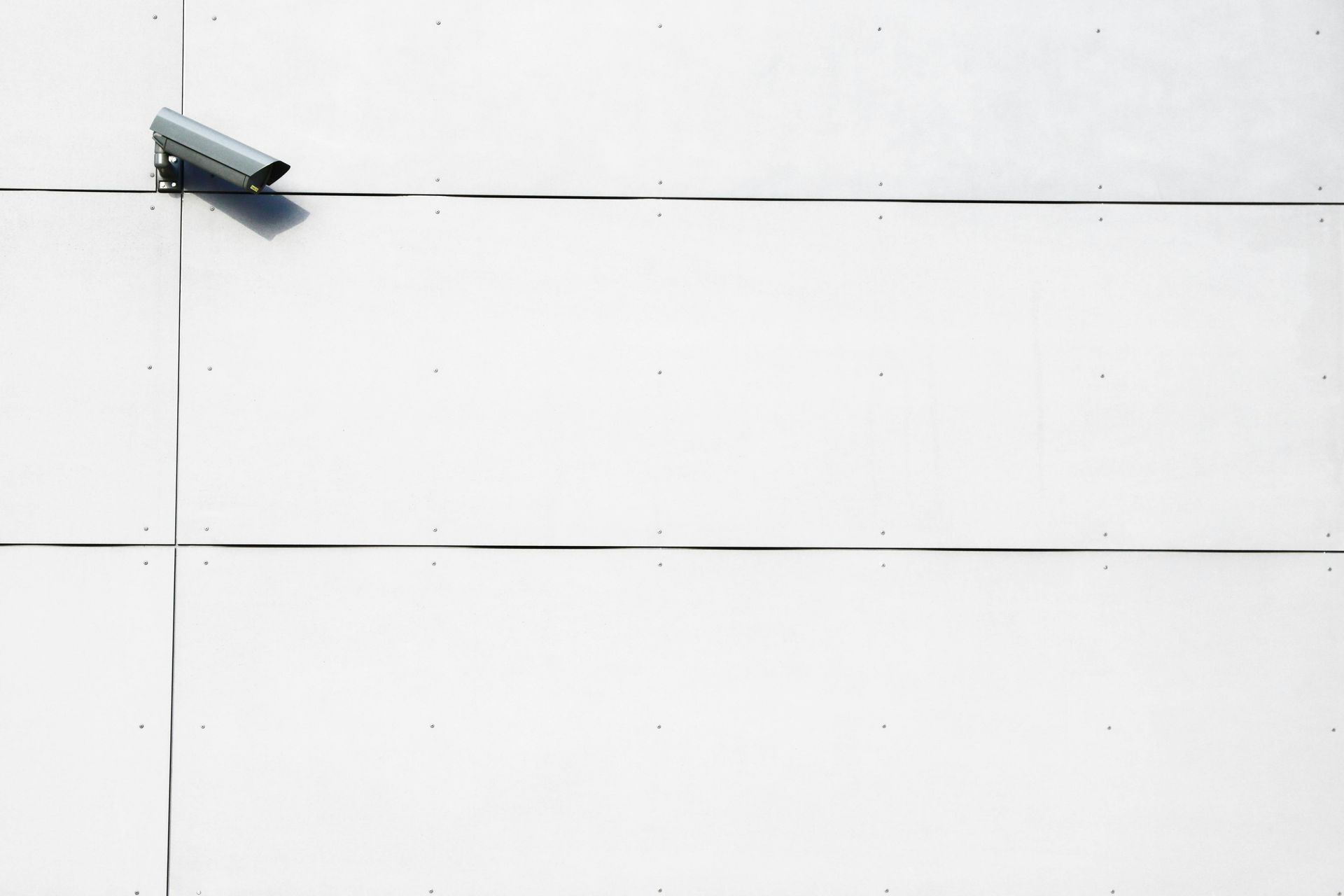 A security camera is sitting on a white tiled wall.