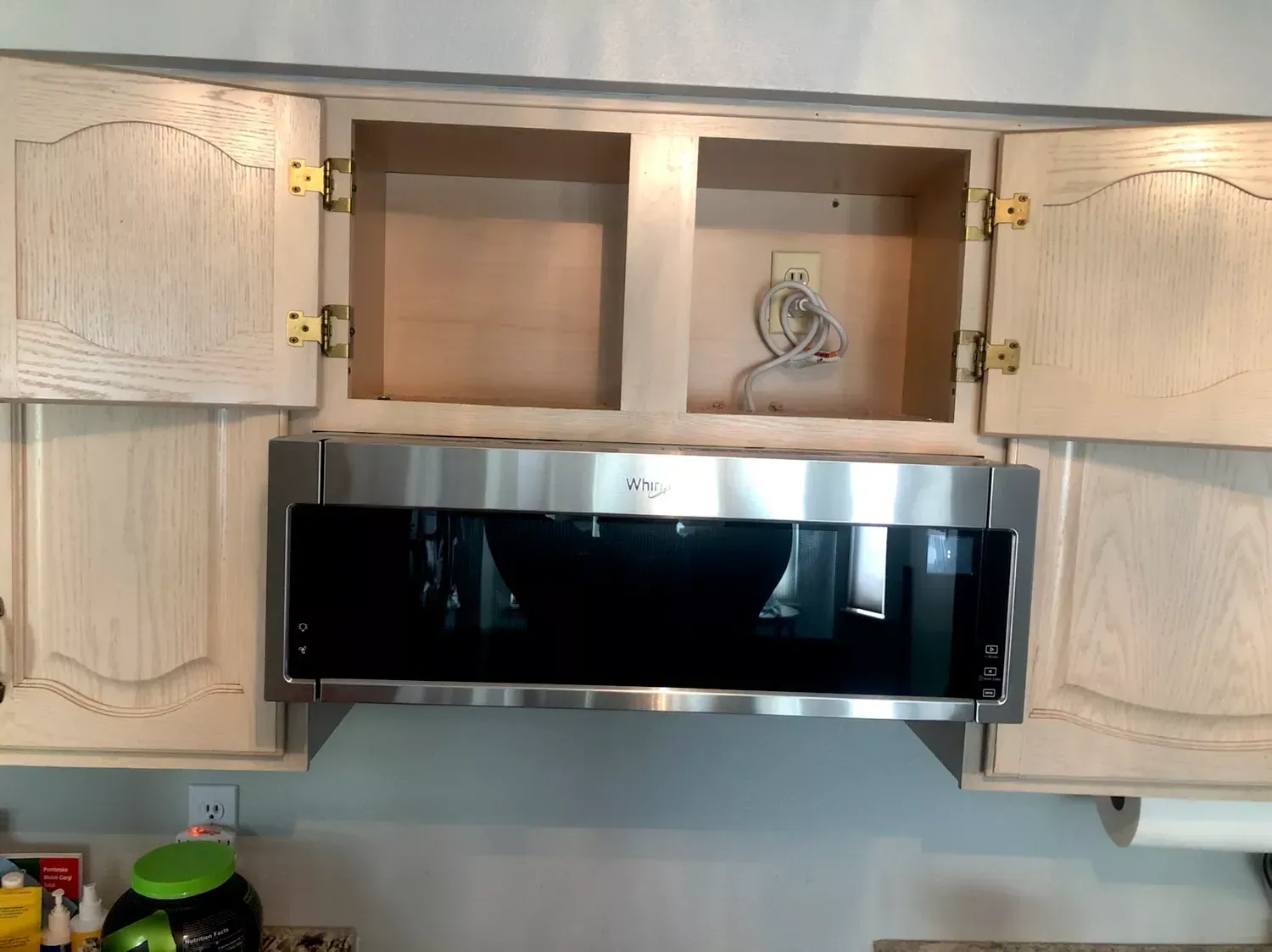 Microwave oven installed under kitchen cabinets, open doors. Silver appliance.
