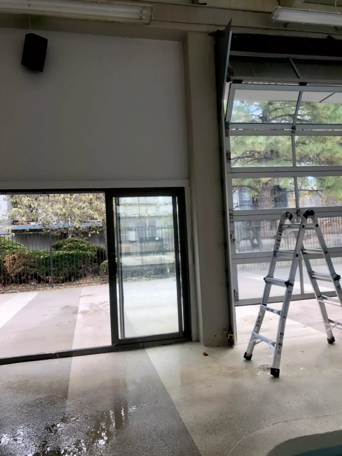 Open glass doors, a ladder, and a partly open garage door inside a building; exterior visible through the openings.