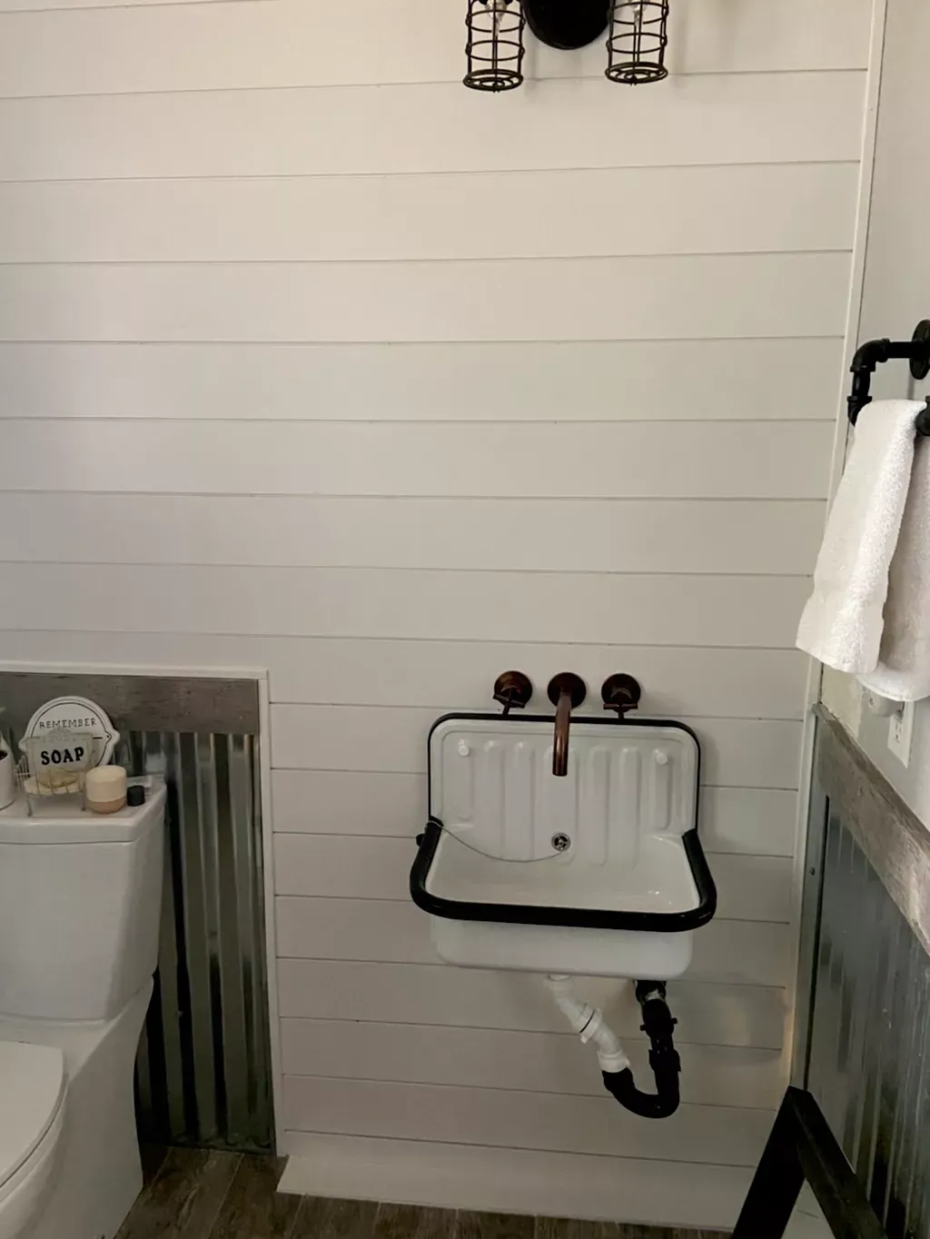 White farmhouse bathroom with a wall-mounted sink, toilet, and metal accent wall.
