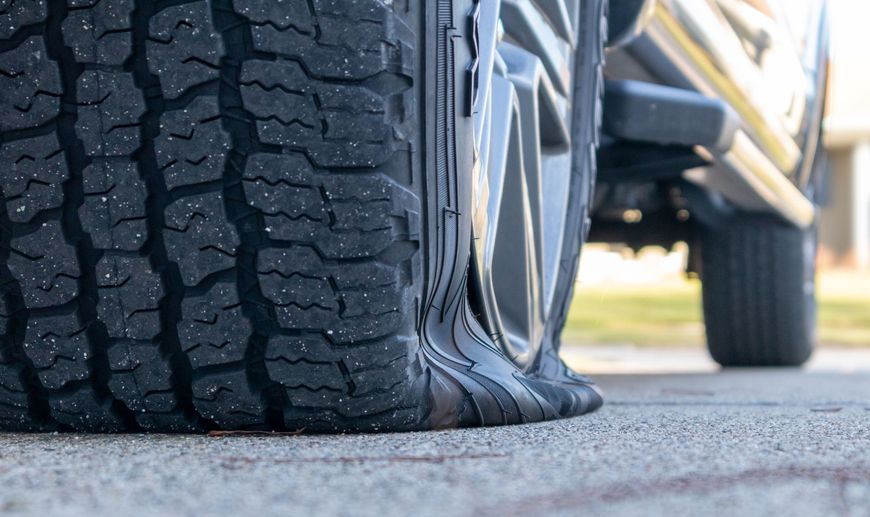 A flat tire on a black truck parked on concrete pavement.