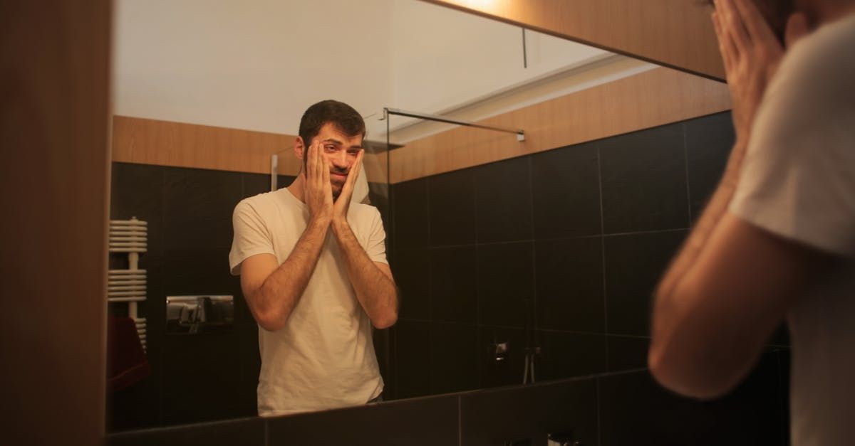 A man is looking at himself in a bathroom mirror.