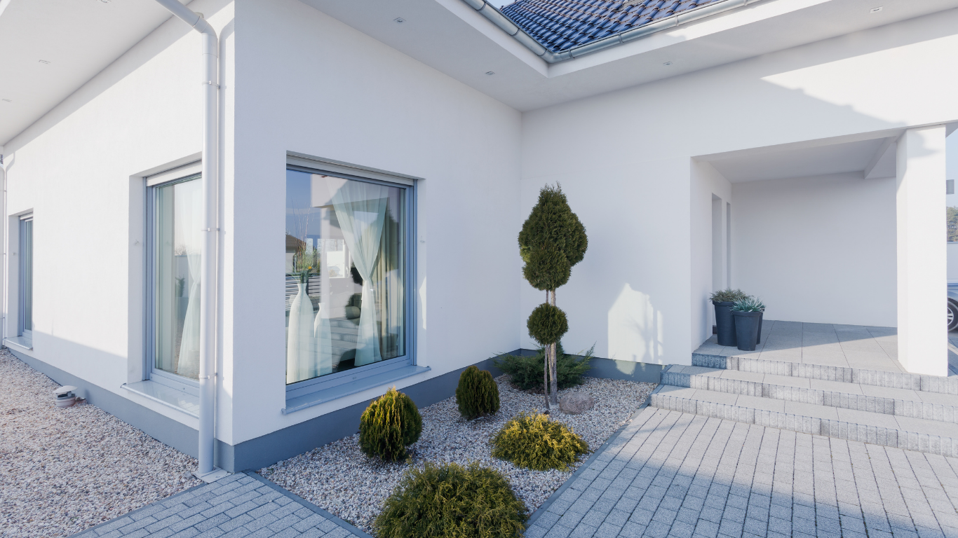 Exterior of a modern, white house with a small garden, gray trim, and a paved entrance.