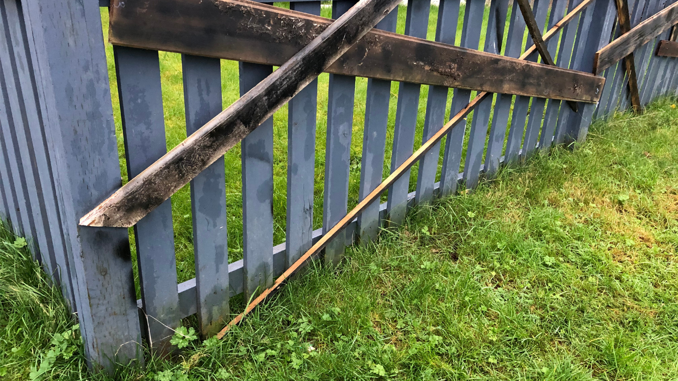 Gray wooden fence with a broken top rail, set against green grass.