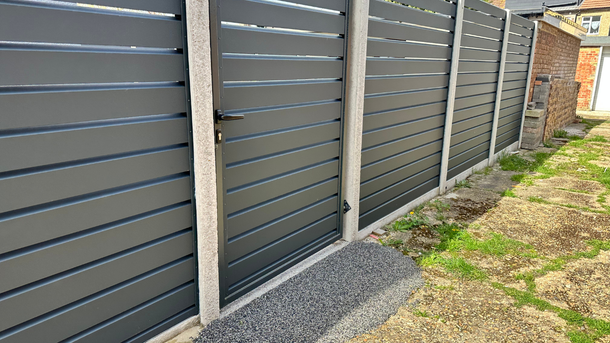 Gray horizontal slat fence with gate, concrete posts, and brick wall.