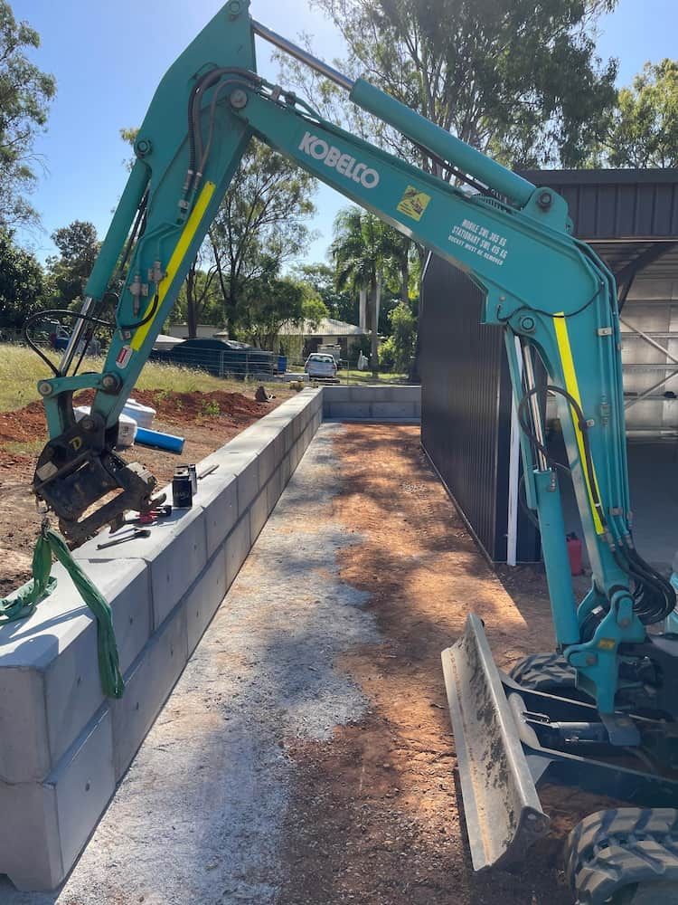 Teal Excavator Placing Concrete Blocks Next to a Building — LS Plant Hire in Calliope, QLD