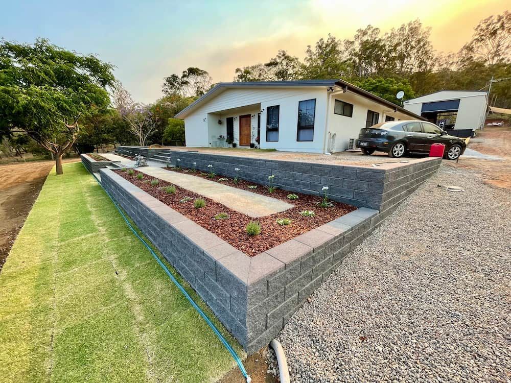 A House With a Retaining Wall, Garden Beds, and a Car in the Driveway on a Sunny Day — LS Plant Hire in Calliope, QLD