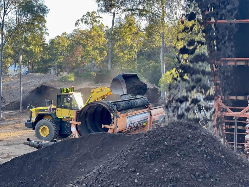 Yellow Loader Moving Dark Compost Near a Large Composter — LS Plant Hire in Calliope, QLD