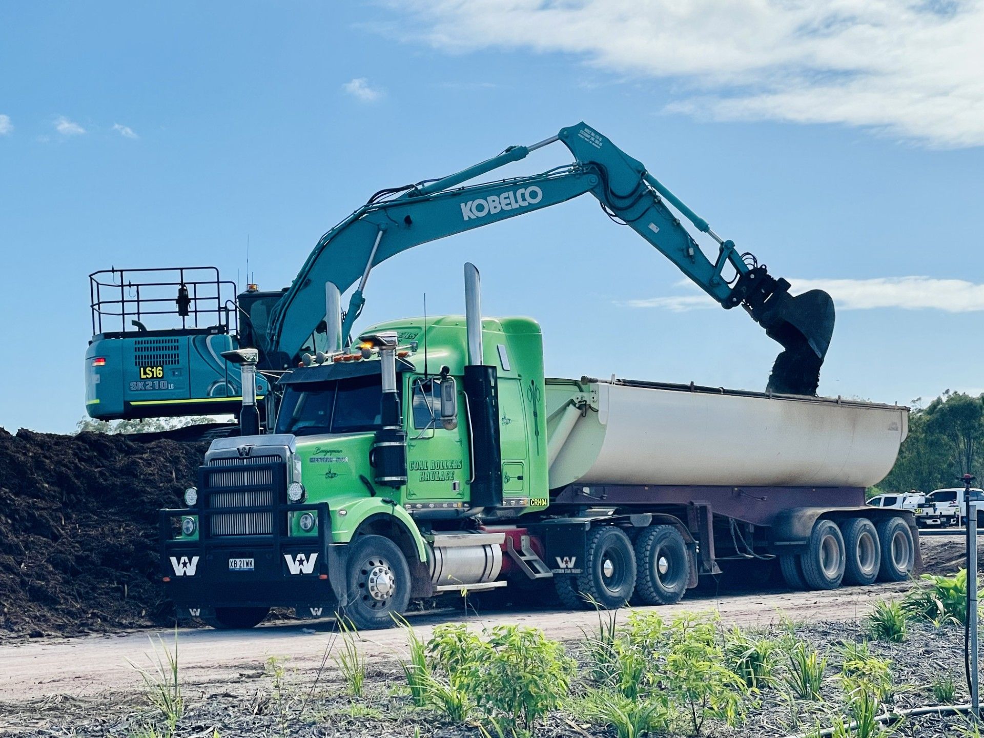 Yellow Excavator Loading Material Into a White Truck Bed Against a Blue Sky — LS Plant Hire in Calliope, QLD