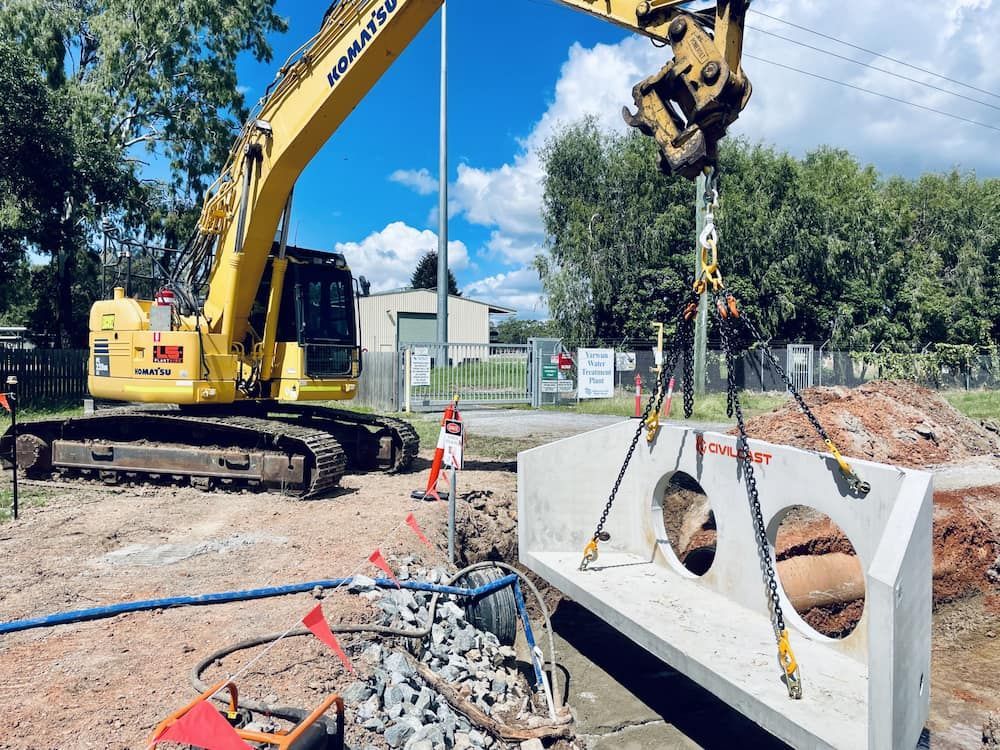 Yellow Excavator Lifts a Concrete Structure With Three Holes, Near a Construction Site — LS Plant Hire in Calliope, QLD
