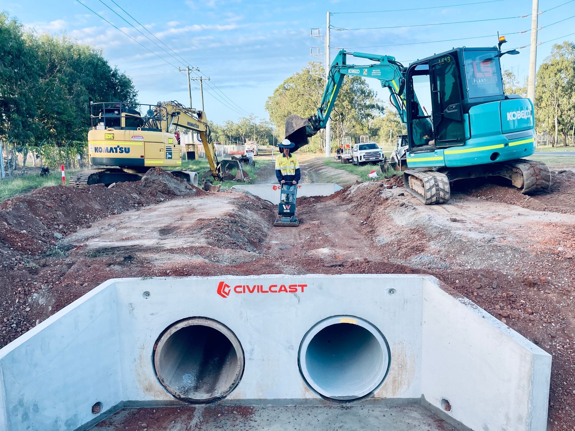 A construction site featuring two excavators, a worker using a compactor, and a large concrete culvert with twin pipes. — LS Plant Hire in Calliope, QLD