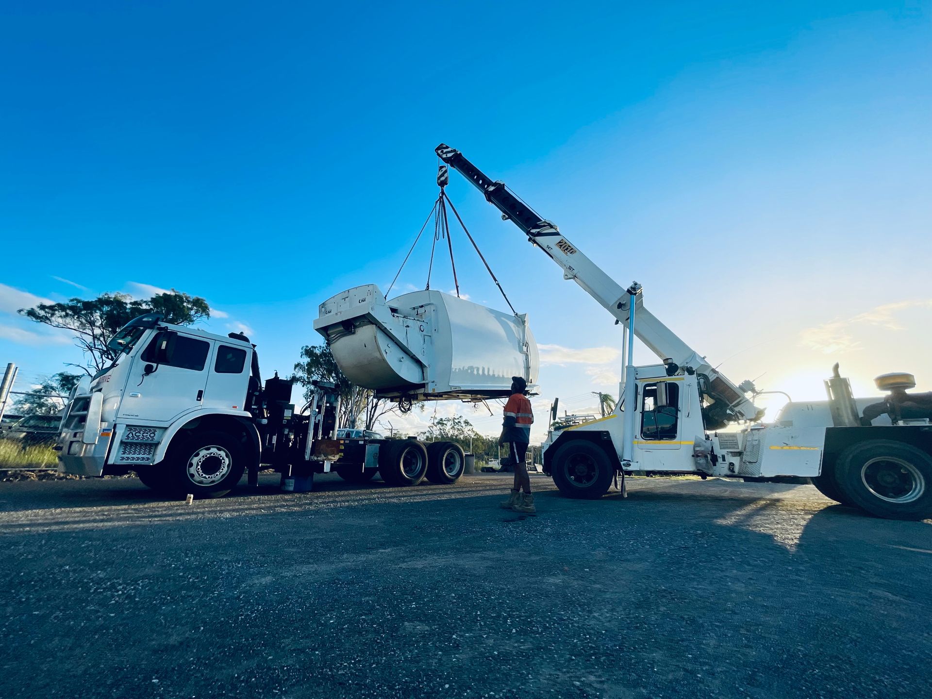 A crane lifts a large white industrial component above a flatbed truck on a sunny day at an outdoor work site. — LS Plant Hire in Calliope, QLD