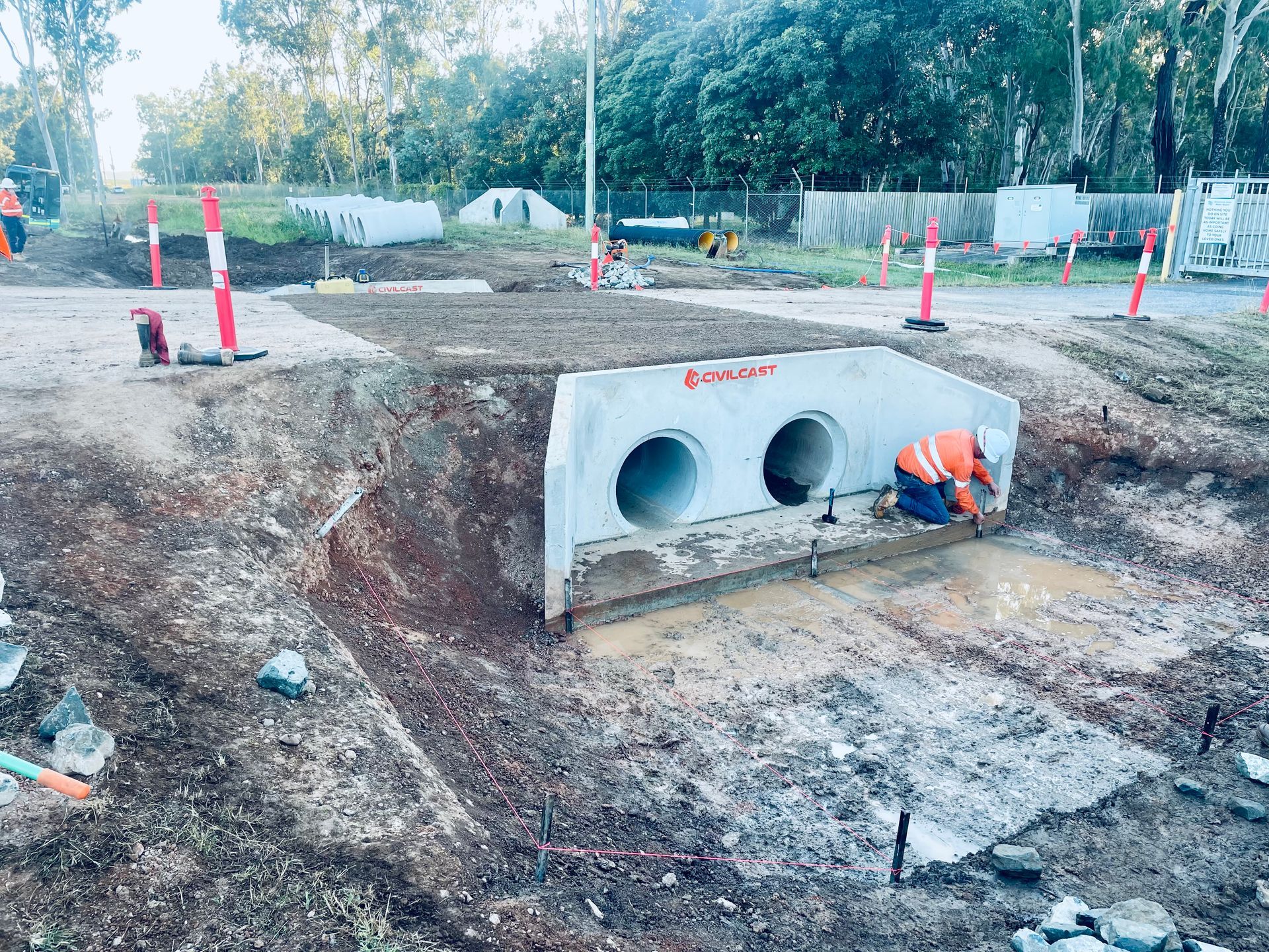 A construction worker in an orange vest kneels by a double concrete culvert being installed at an outdoor job site. — LS Plant Hire in Calliope, QLD