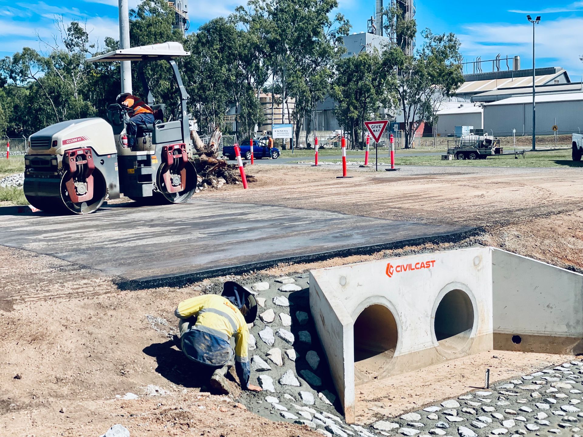 A worker in a high-visibility shirt finishes a stone-lined drainage area near a road roller at a construction site. — LS Plant Hire in Calliope, QLD