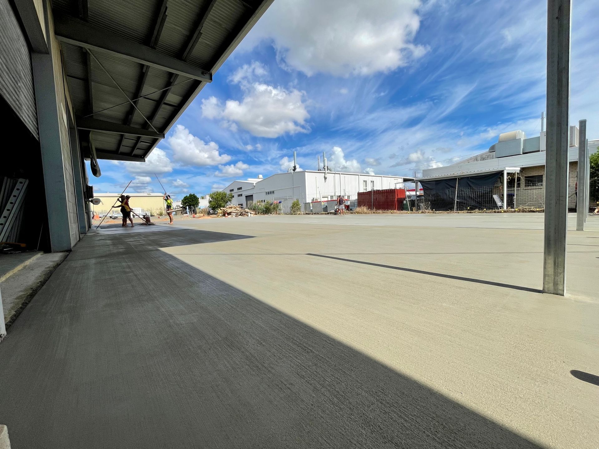 Workers use tools to smooth a large, freshly poured concrete surface under a shed roof on a sunny day. — LS Plant Hire in Calliope, QLD