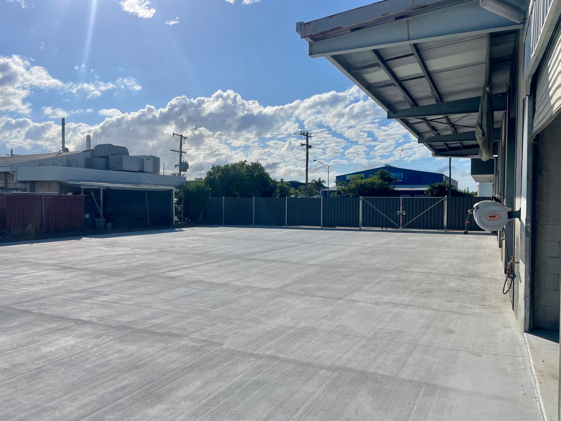 A wide, concrete open-air yard area beside a warehouse with a metal awning under a bright, sunny sky. — LS Plant Hire in Calliope, QLD