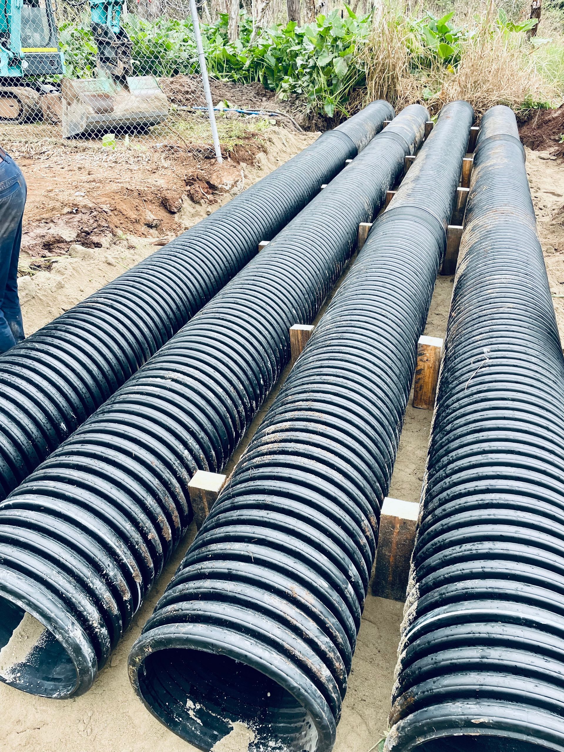 Four black corrugated plastic drainage pipes laid in parallel rows on a dirt construction site. — LS Plant Hire in Calliope, QLD